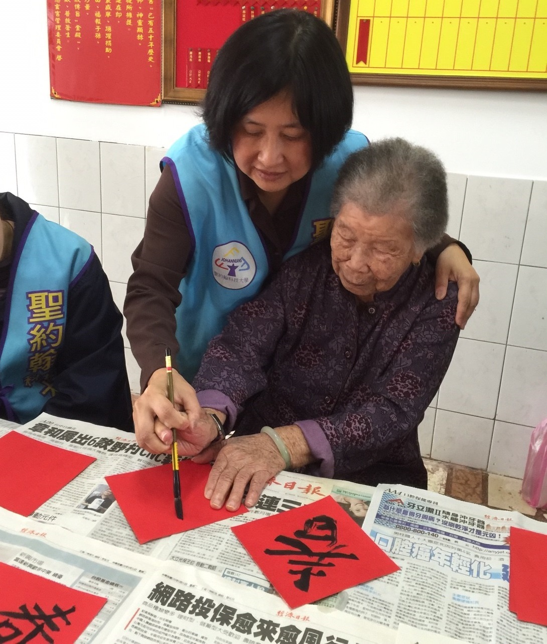 賈大齡組長握住高齡96歲陳姓阿嬤的手一筆一畫的寫春聯，讓不識字且手僵硬的阿嬤覺得滿足及感動