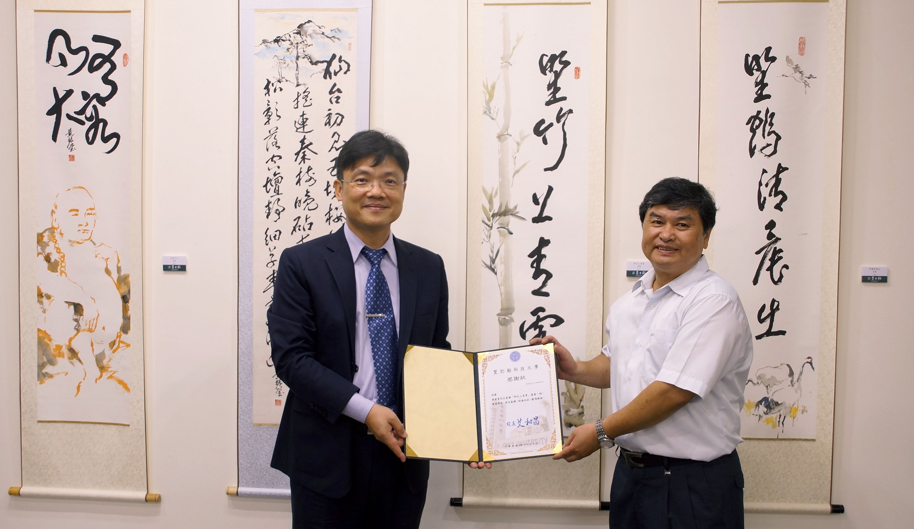 黃振瑩藝術家（右）得知聖約翰校徽裡的竹子代表上海聖約翰大學，特別致贈「野竹上青霄」書畫一幅，提供藝文中心典藏，艾和昌校長（左）致贈感謝狀表達感謝