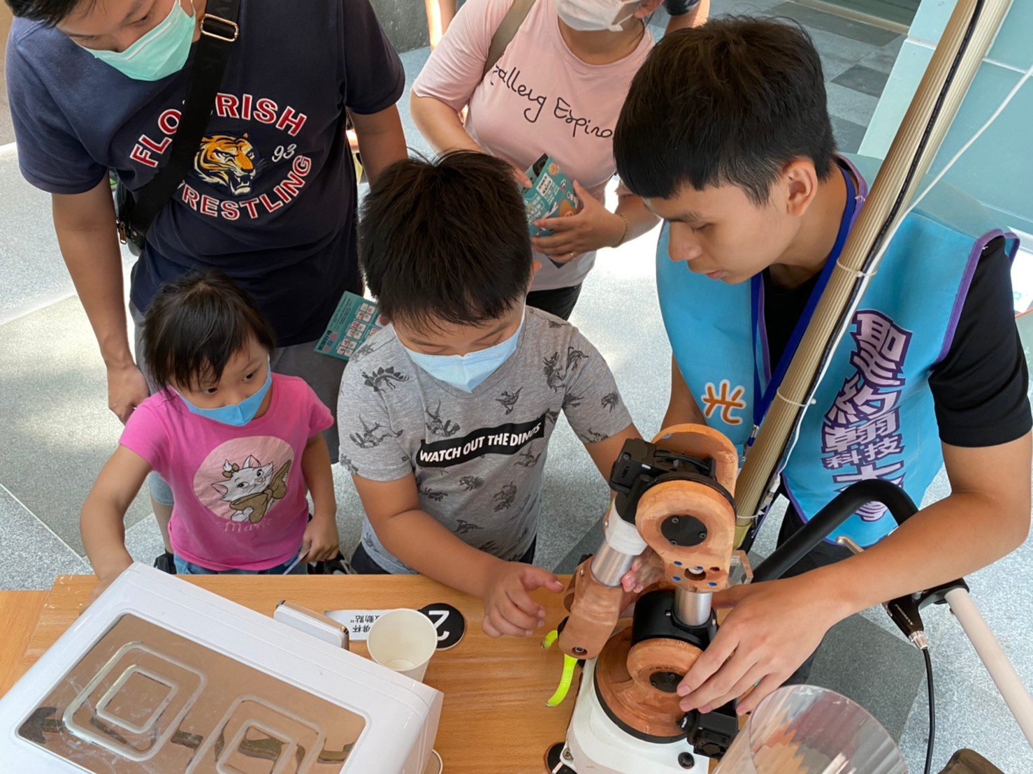 聖約翰科大工管系陳家樂同學（右一）教導現場小朋友學習操作機器手臂夾取紙杯。